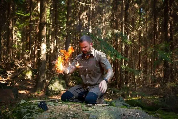 Person zündet Feuer in einem Waldgebiet beim Survival Training