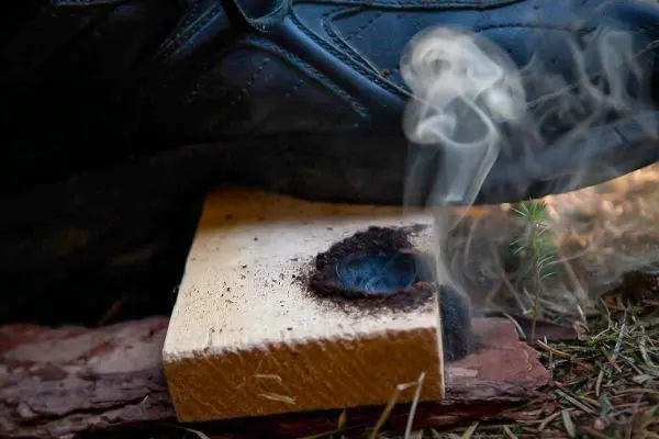 Rauch steigt von einem Holzstück auf, während ein Schuh darauf drückt