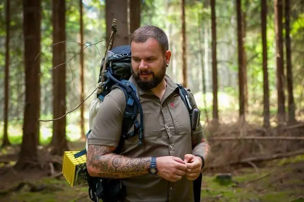 Rucksack mit Ausrüstung auf dem Rücken, steht im Wald zwischen Bäumen