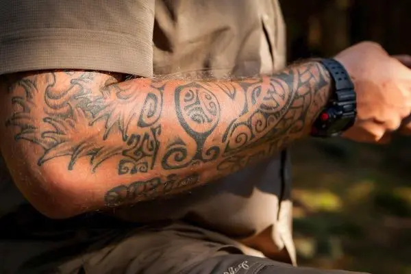 Tatowierte Arm mit verschiedenen Mustern und Designs, Hand hält ein Objekt