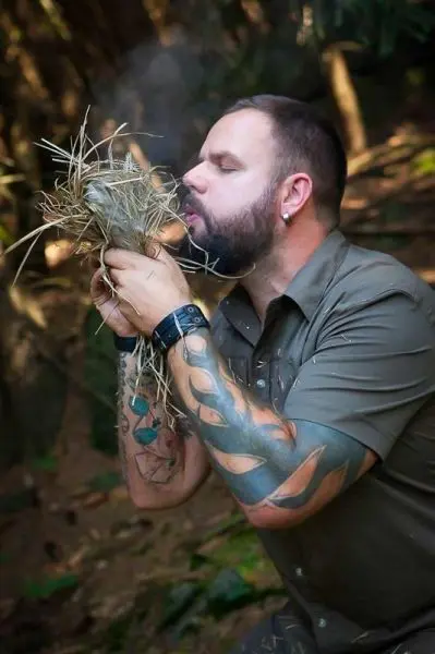 Zunder glimmt in den Händen, während Luft zugeführt wird