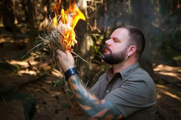 Zunder glimmt in Händen, kleine Flamme entsteht im Wald