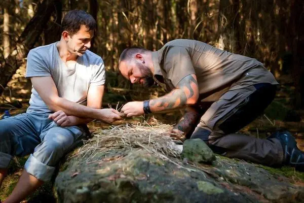 Zunder wird auf einem Stein vorbereitet, während zwei Personen konzentriert arbeiten