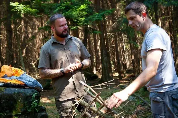 Zwei Männer arbeiten im Wald an einer Holzstruktur aus Ästen