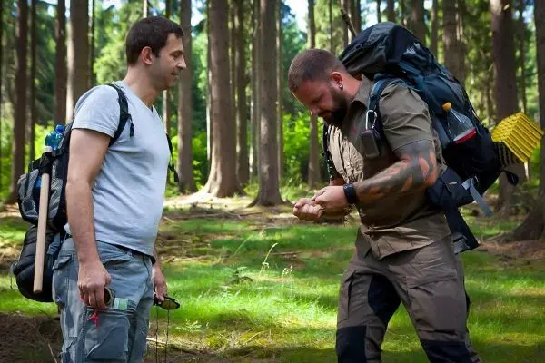 Zwei Männer im Wald, einer mit Rucksack, der andere beobachtet