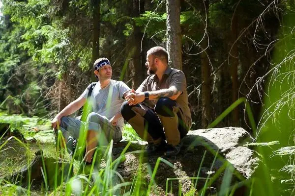 Zwei Männer sitzen auf einem Felsen im Wald und unterhalten sich