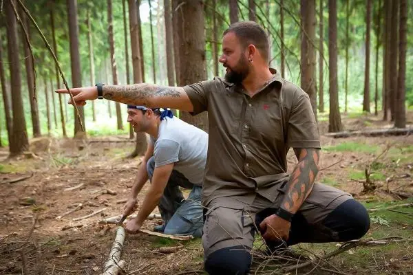 Zwei Personen im Wald, eine kniet und zeigt auf etwas, die andere sammelt Äste