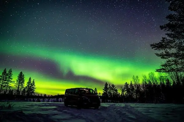 Dunkler Himmel mit Sternen und grünem Polarlicht über schneebedecktem Boden und einem Fahrzeug