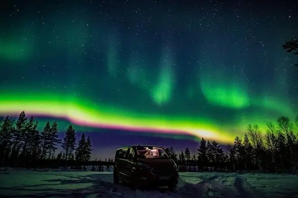 Fahrzeug steht im Schnee unter dem Nordlicht und Sternenhimmel