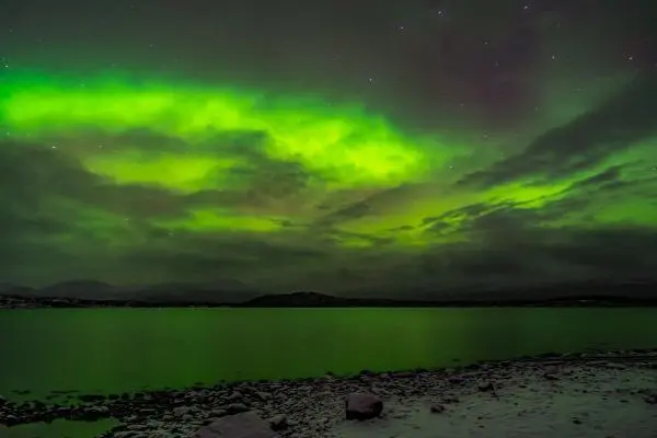 Grüne Aurora über einem ruhigen Gewässer mit Steinen am Ufer