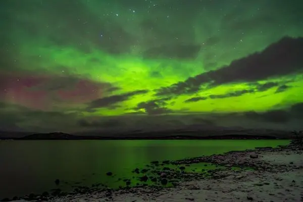 Grüne Aurora über einem ruhigen Gewässer mit steiniger Uferlinie