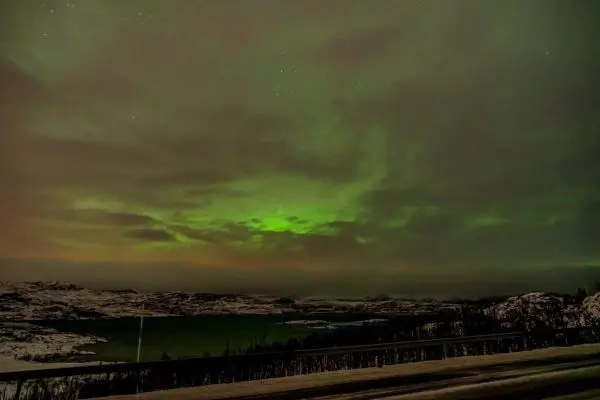 Grüne Lichtstrahlen durchziehen bewölkten Nachthimmel über einer winterlichen Landschaft