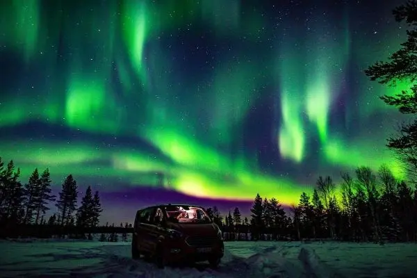 Grünes Polarlicht leuchtet über verschneiter Landschaft und einem parkenden Fahrzeug