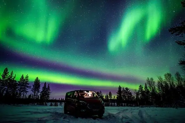 Nordlichter leuchten über einem Fahrzeug in verschneiter Landschaft