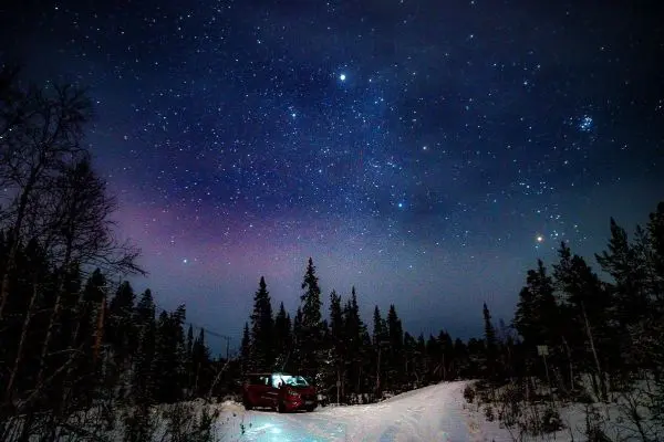 Roter Van steht auf einem verschneiten Weg unter einem sternenklaren Nachthimmel