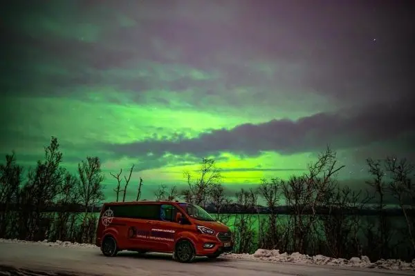 Roter Van steht auf einer schneebedeckten Straße unter grünem Polarlicht