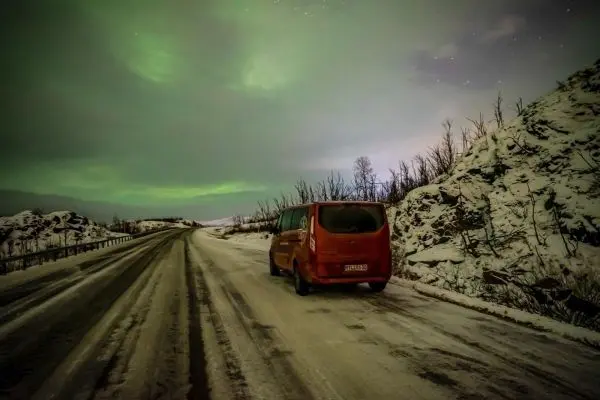 Roter Van steht auf einer verschneiten Straße unter grünem Polarlicht