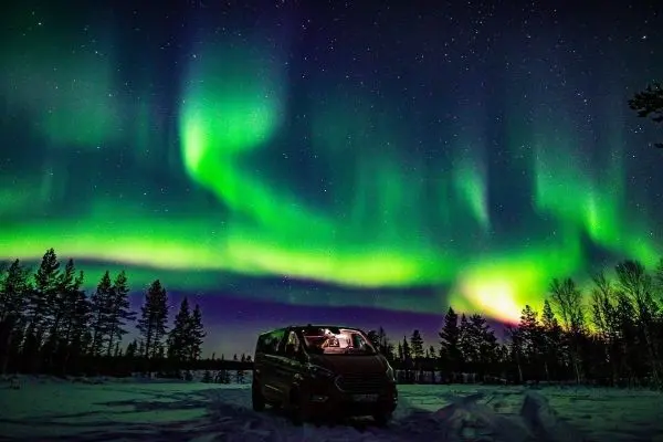 Roter Van steht im Schnee unter dem Nordlicht mit grünen und blauen Farben