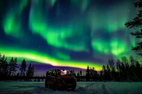 Roter Van steht im Schnee unter dem Nordlicht mit grünen und lila Farben