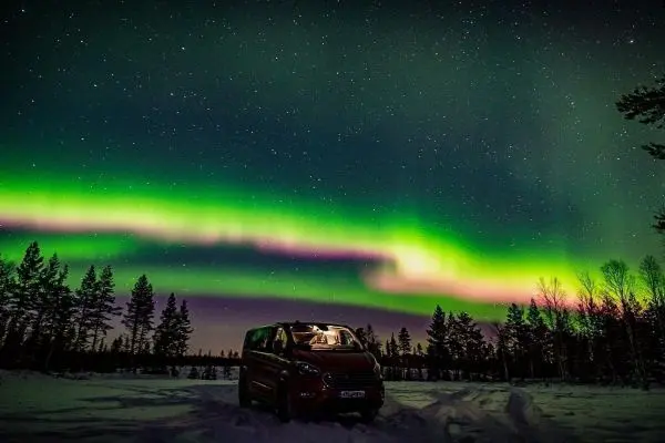 Roter Van steht im Schnee unter dem Nordlicht und Sternenhimmel
