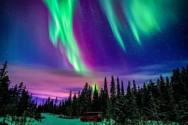 Sternenhimmel mit bunten Polarlichtern über schneebedecktem Wald und Straße