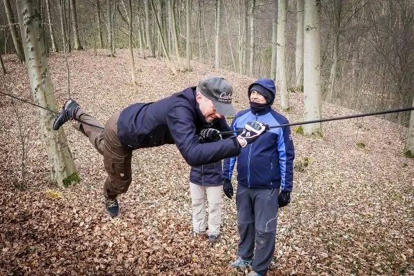 Mann überquert selbstgebaute Seilbrücke, während zwei Personen beobachten