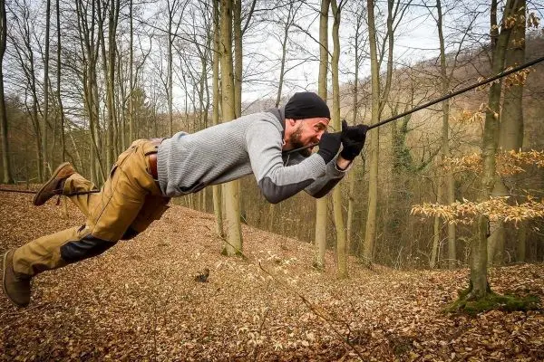 Mann überquert selbstgebaute Seilbrücke zwischen Bäumen im Wald