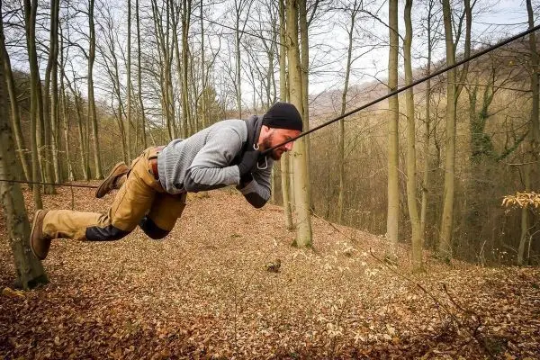 Mann überquert selbstgebaute Seilbrücke zwischen Bäumen im Wald