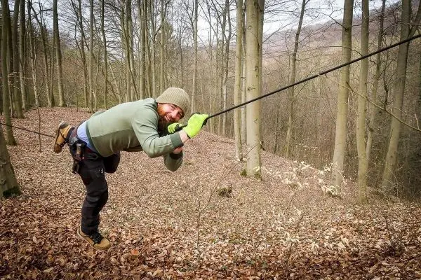 Mann überquert selbstgebaute Seilbrücke zwischen Bäumen im Wald