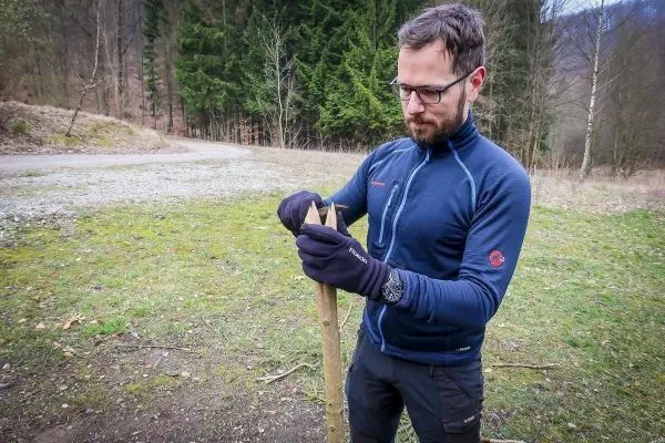 Person bearbeitet einen Stock mit einem Messer beim Überlebenstraining