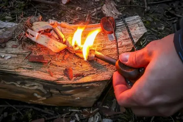 Person entzündet Feuer mit einem Feuerzeug auf einem Holzstück beim Survival Training