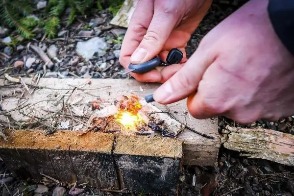 Person entzündet Feuer mit Feuerstahl auf Holzstück