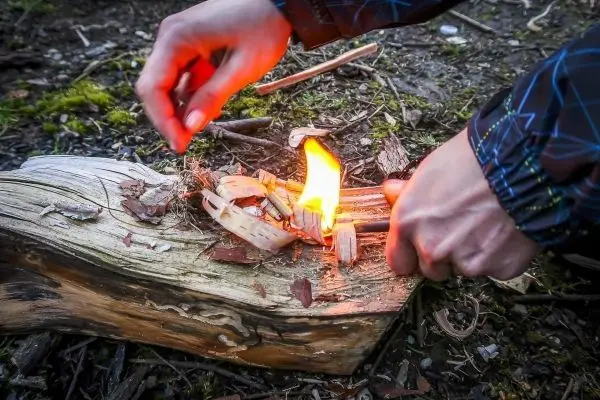Person entzündet Feuer mit Zunder auf Holzstück beim Survival Training