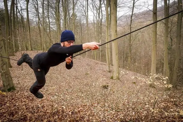 Person schwingt an einer selbstgebauten Seilbrücke durch den Wald