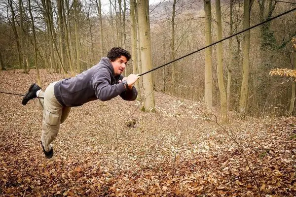 Person schwingt an Seil zwischen Bäumen im Wald