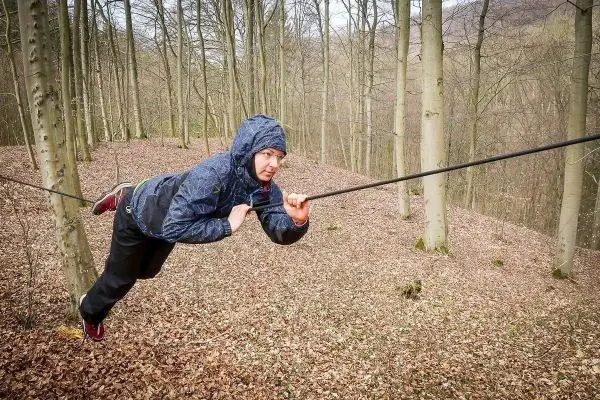 Person schwingt an selbstgebauter Seilbrücke zwischen Bäumen