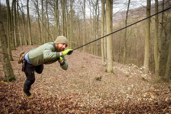 Person zieht sich an einem Seil durch den Wald