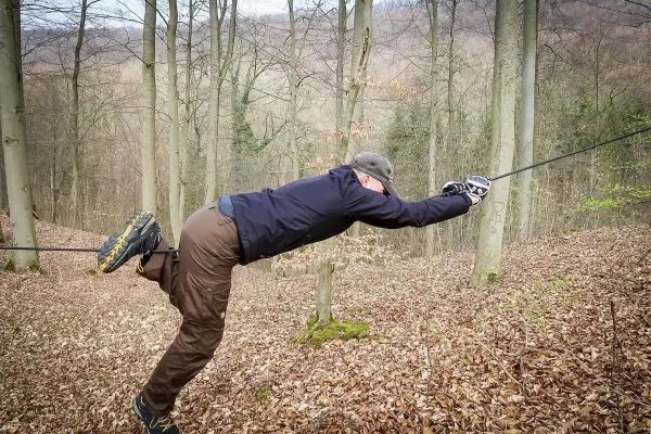 Person zieht sich an einem Seil in den Wald hoch