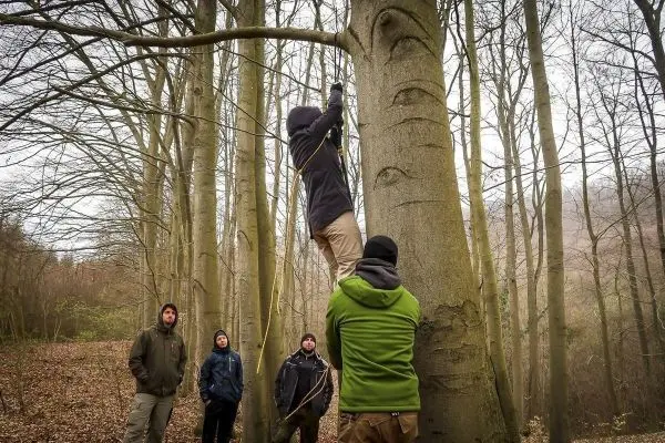 Teilnehmer nutzt Seil, um an Baum zu klettern, während andere beobachten