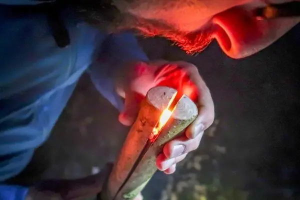 Zunder glimmt in einem gespaltenen Holzstück, während jemand darüber bläst