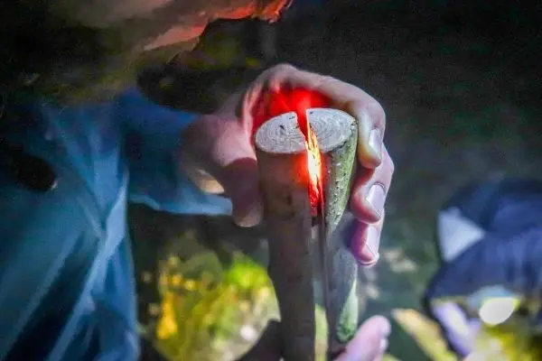Zunder glimmt in einem Holzstück während Feuerstahl Funken erzeugt
