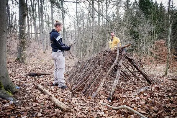 Zwei Personen bauen eine Laubhütte aus Ästen im Wald