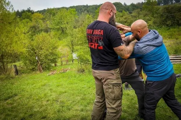 Drei Personen üben eine Selbstverteidigungstechnik im Freien auf einer Wiese