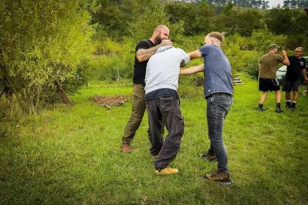 Drei Personen üben eine Selbstverteidigungstechnik im Freien auf einer Wiese