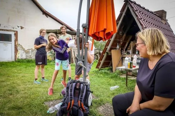 Gruppe von fünf Personen interagiert im Freien, eine Person hält einen Rucksack