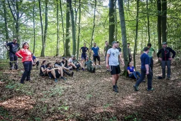 Gruppe von Personen sitzt und steht im Wald auf Laub