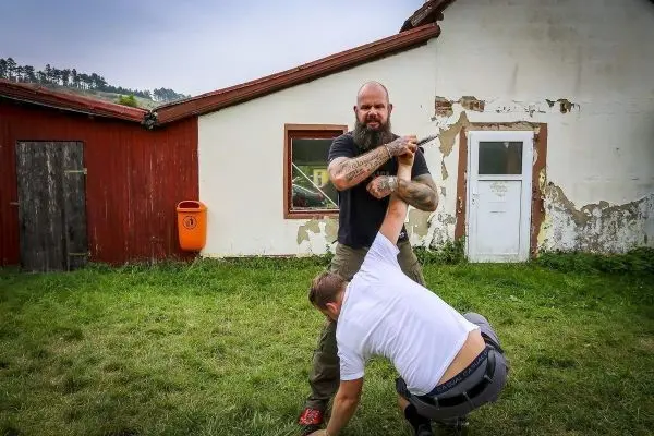 Kämpfer kontrolliert Gegner im Haltegriff auf einer Wiese vor einem Gebäude