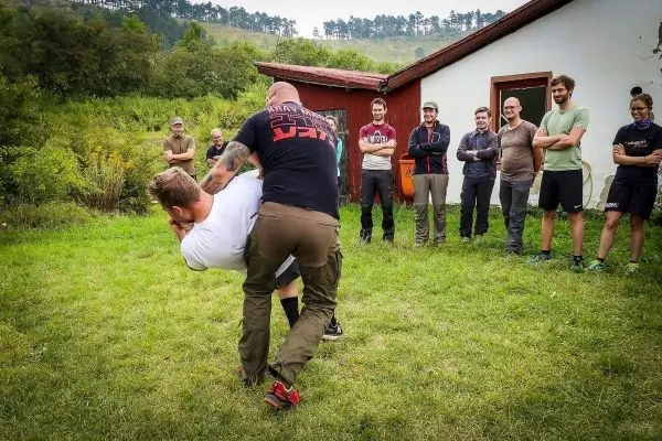 Kampftechniken werden in einer Trainingssituation demonstriert, Zuschauer beobachten aufmerksam