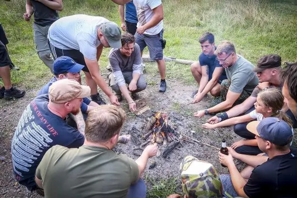 Kleines Bodenfeuer umringt von mehreren Personen, die mit Stöcken hantieren