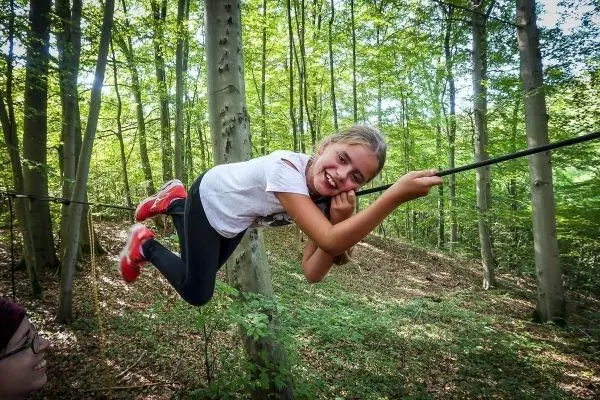 Mädchen überquert selbstgebaute Seilbrücke zwischen Bäumen im Wald